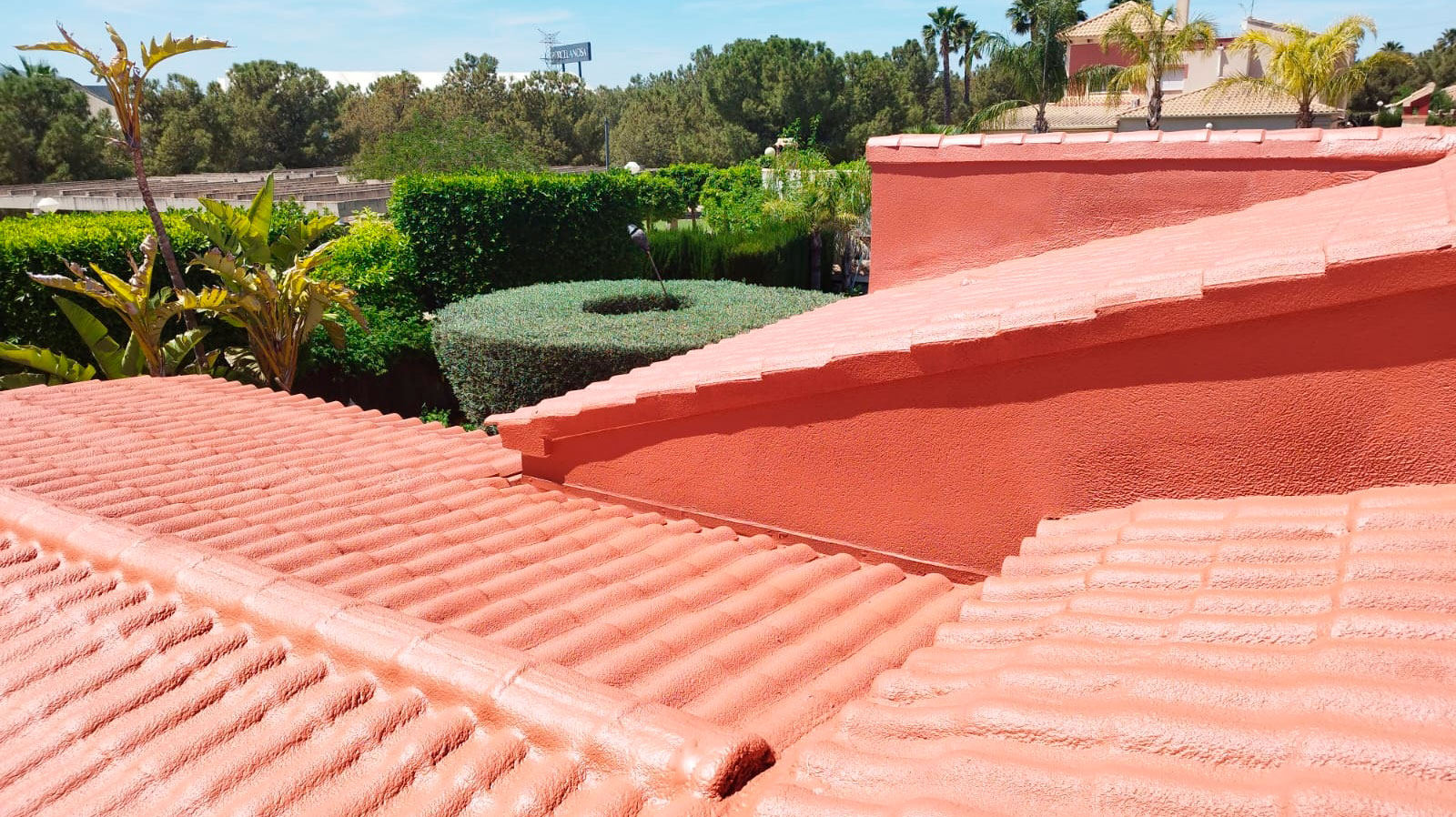 Cubierta de teja cerámica pintada en terracota tras impermeabilización y renovación, con jardín y palmeras al fondo