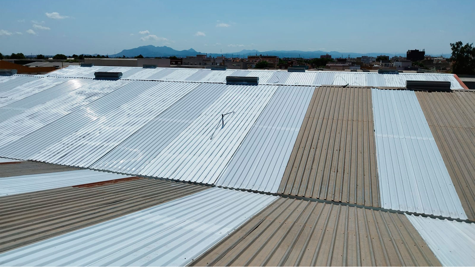Cubierta industrial renovada con chapa metálica nueva en Murcia, con lucernarios y montañas al fondo