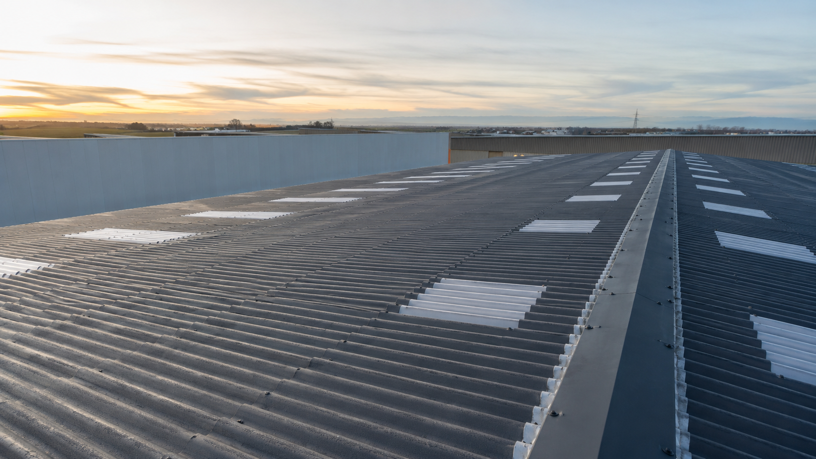 Cubierta industrial de chapa ondulada gris con lucernarios translúcidos al atardecer, renovada por OBRASOC